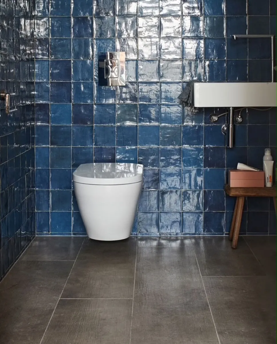 Toilet met blauwe handvormtegels en een betonlook vloer.